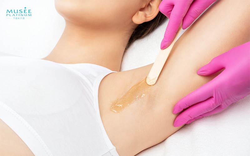 Beautician applying wax to woman underarm